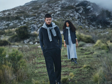 Man and woman wearing winter alpaca clothing while walking on a grassy mountain landscape in Peru.